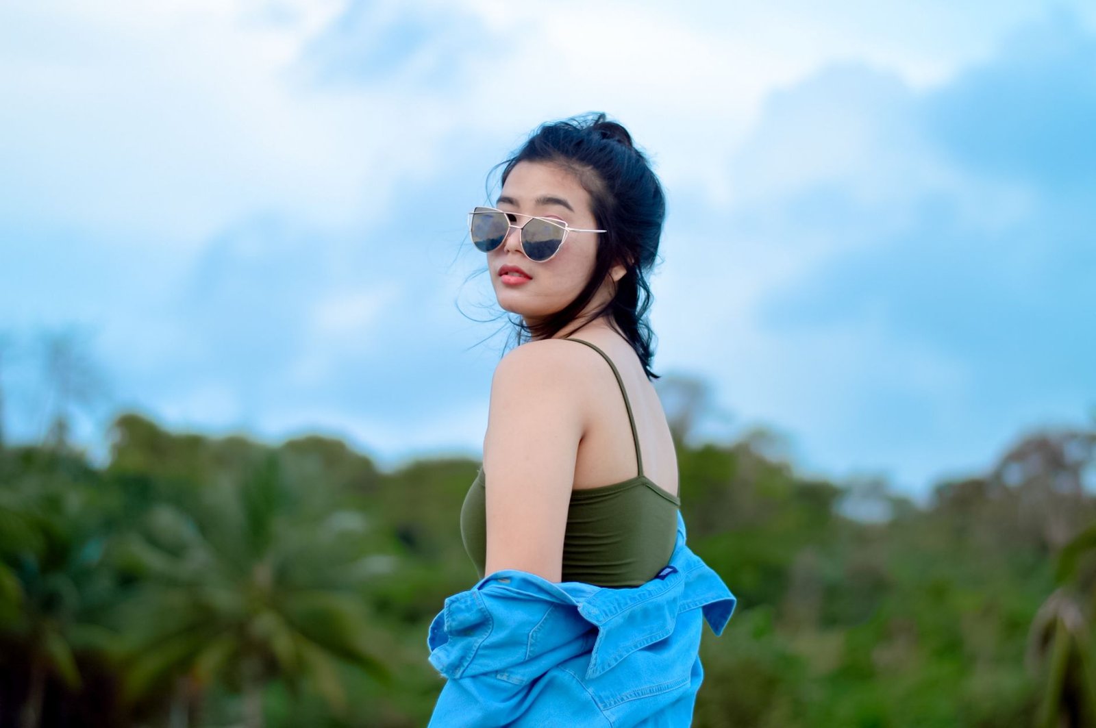 woman in sunglasses standing on field in front of line of trees