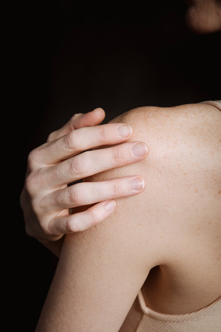 slim female touching shoulder against dark background