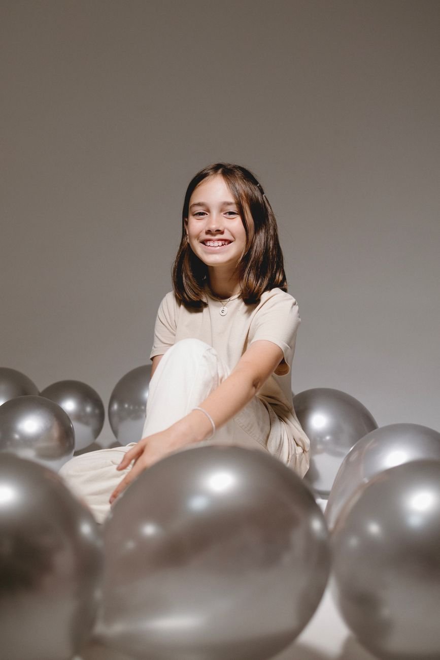 a girl sitting on a bunch of silver balloons