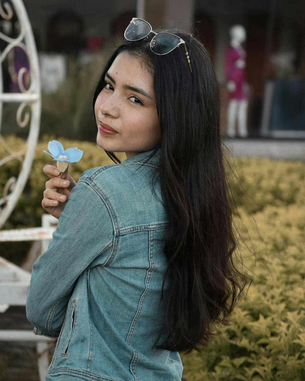 young woman in denim jacket holding blue flower outdoors