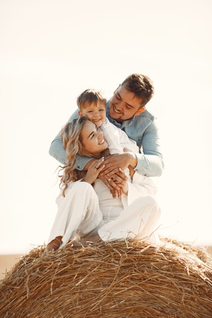 man standing beside woman and boy sitting on hay bale