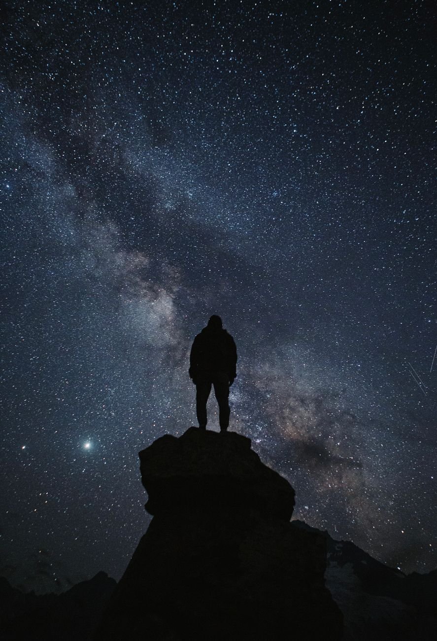 a silhouette of person standing on a rock under the starry sky