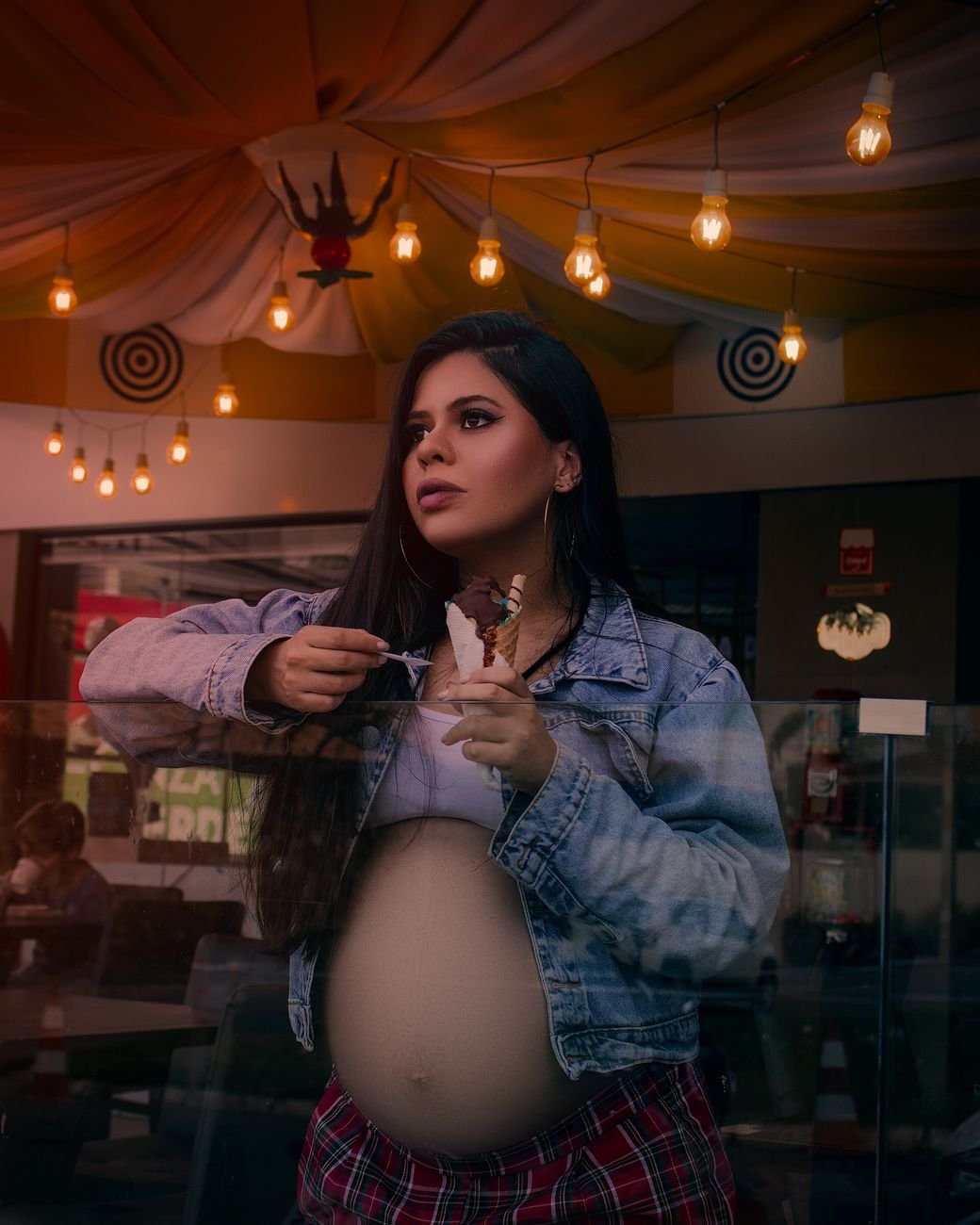 a pregnant woman in a denim jacket holding an ice cream in a cone