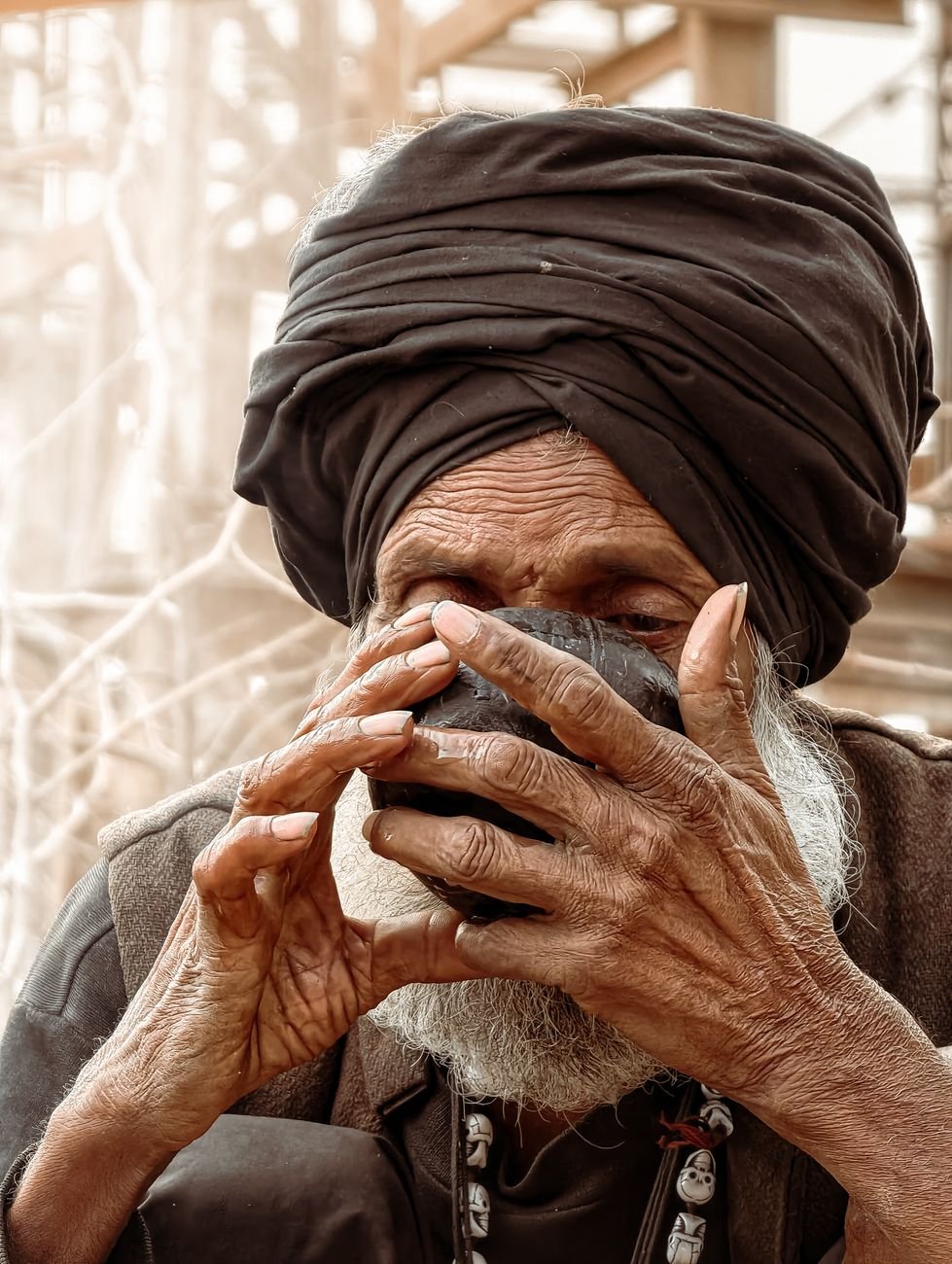 elderly man with turban sipping tea outdoors