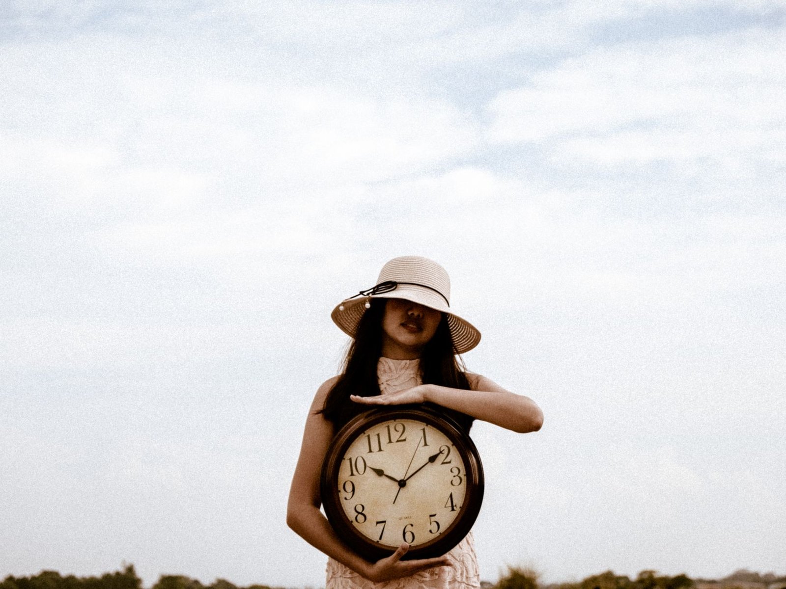 woman holding big clock and wearing hat