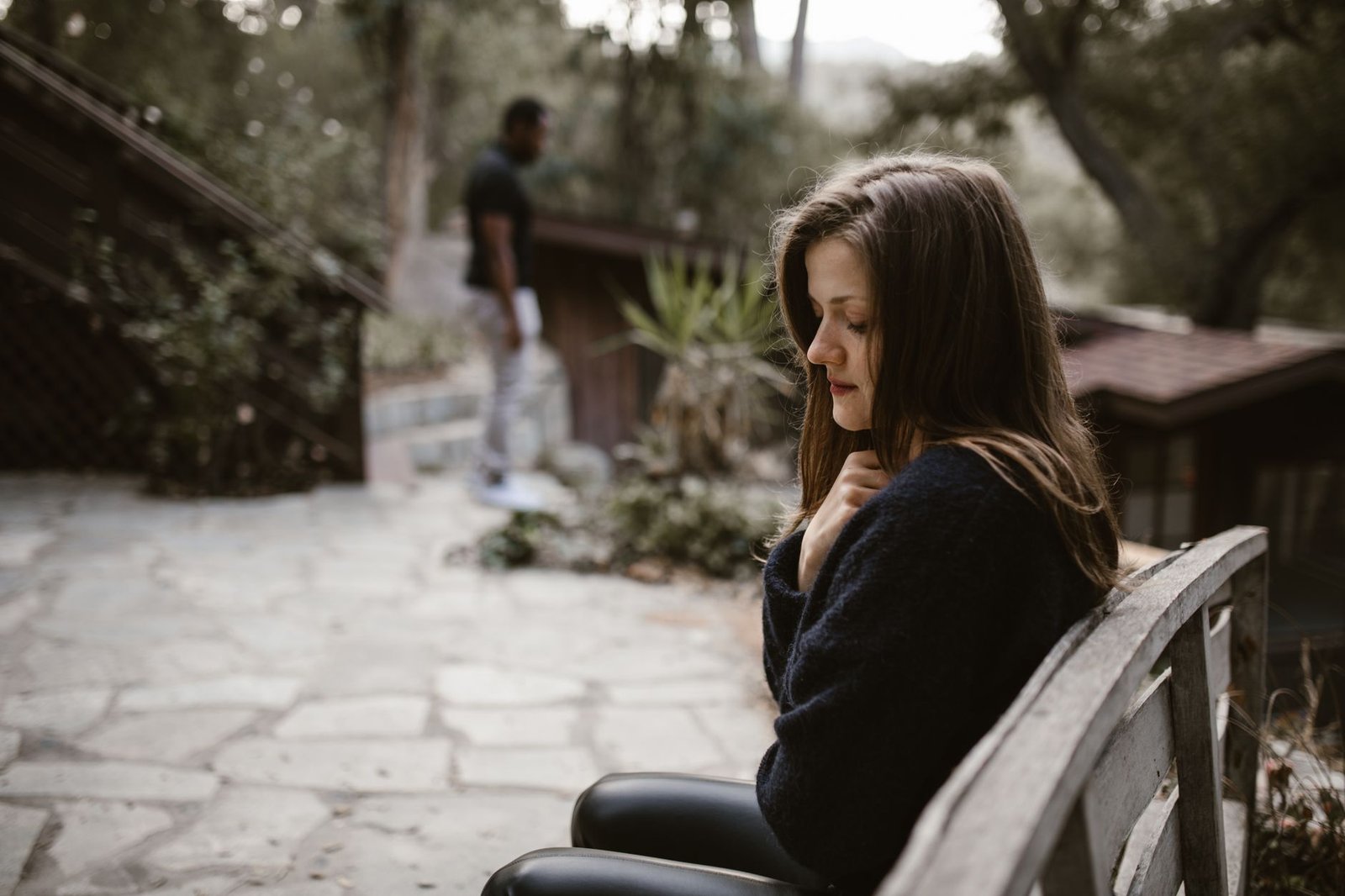 man in black jacket sitting on brown wooden bench
