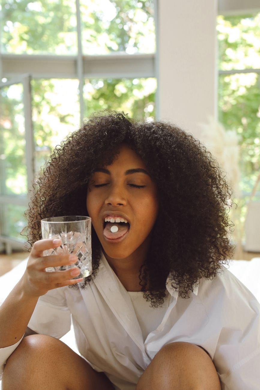 woman holding a drinking glass with a pill on her mouth