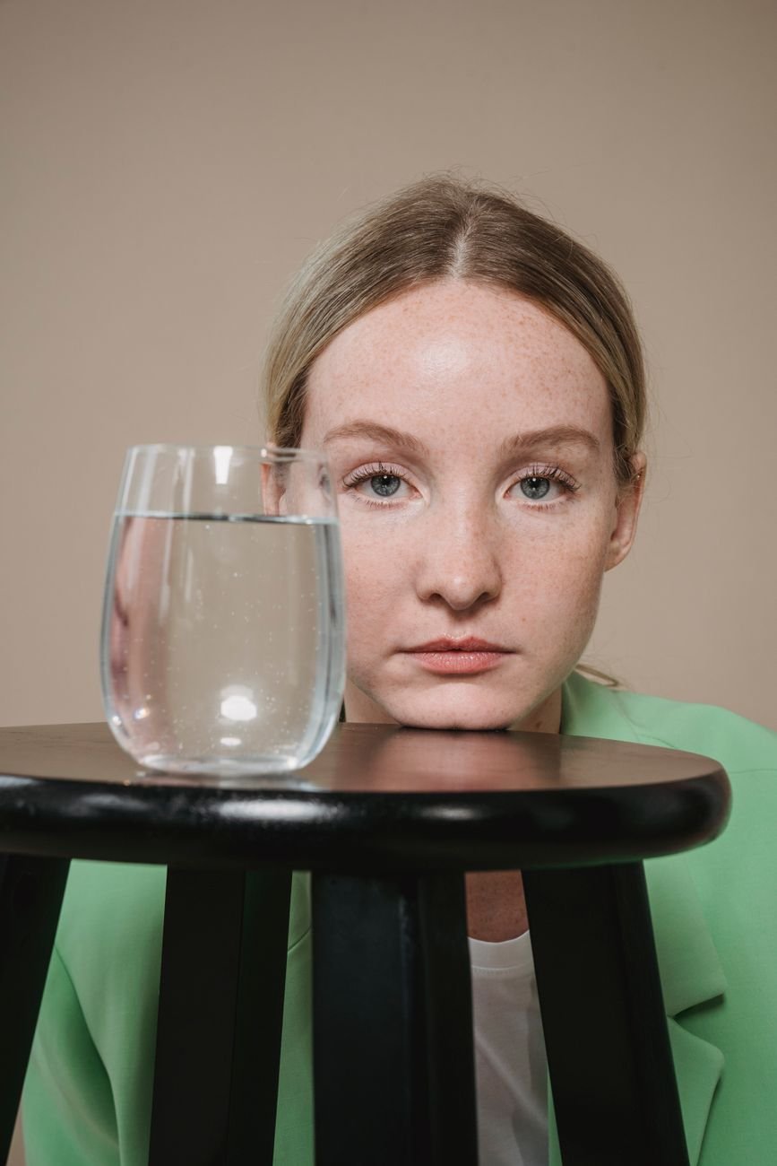 clear drinking glass with liquid near the woman s face