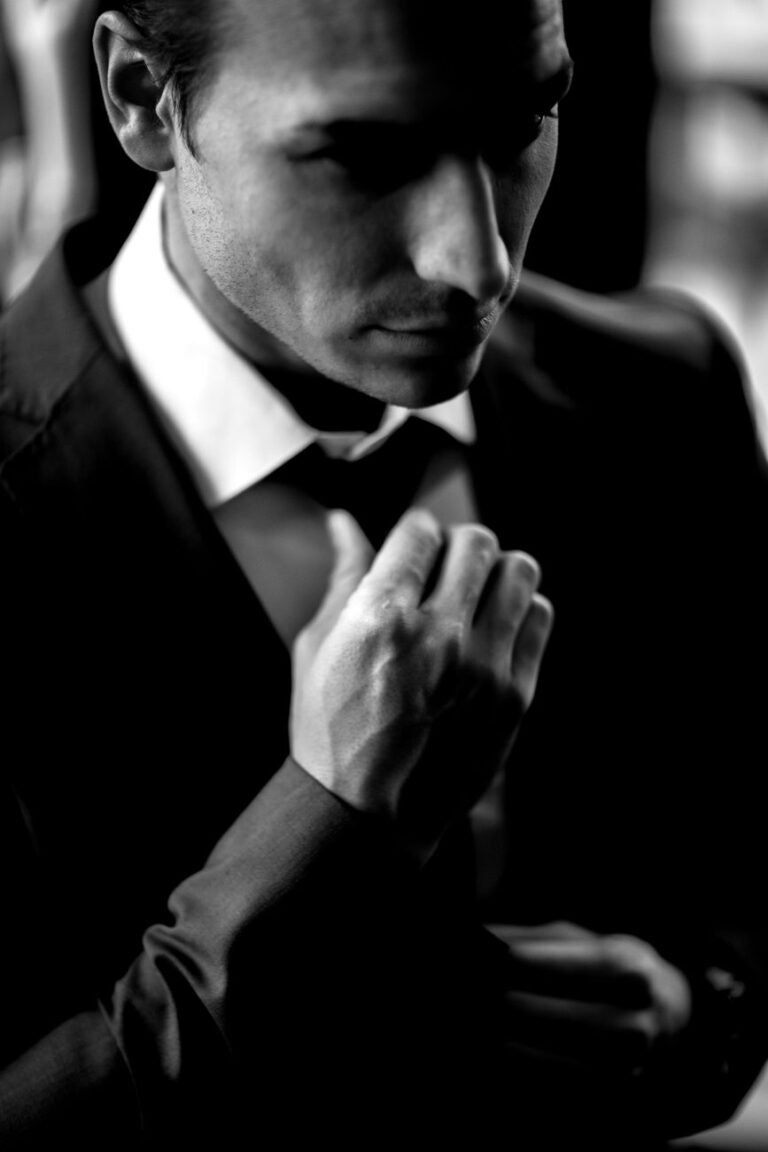 grayscale photo of a handsome man in a suit fixing his necktie