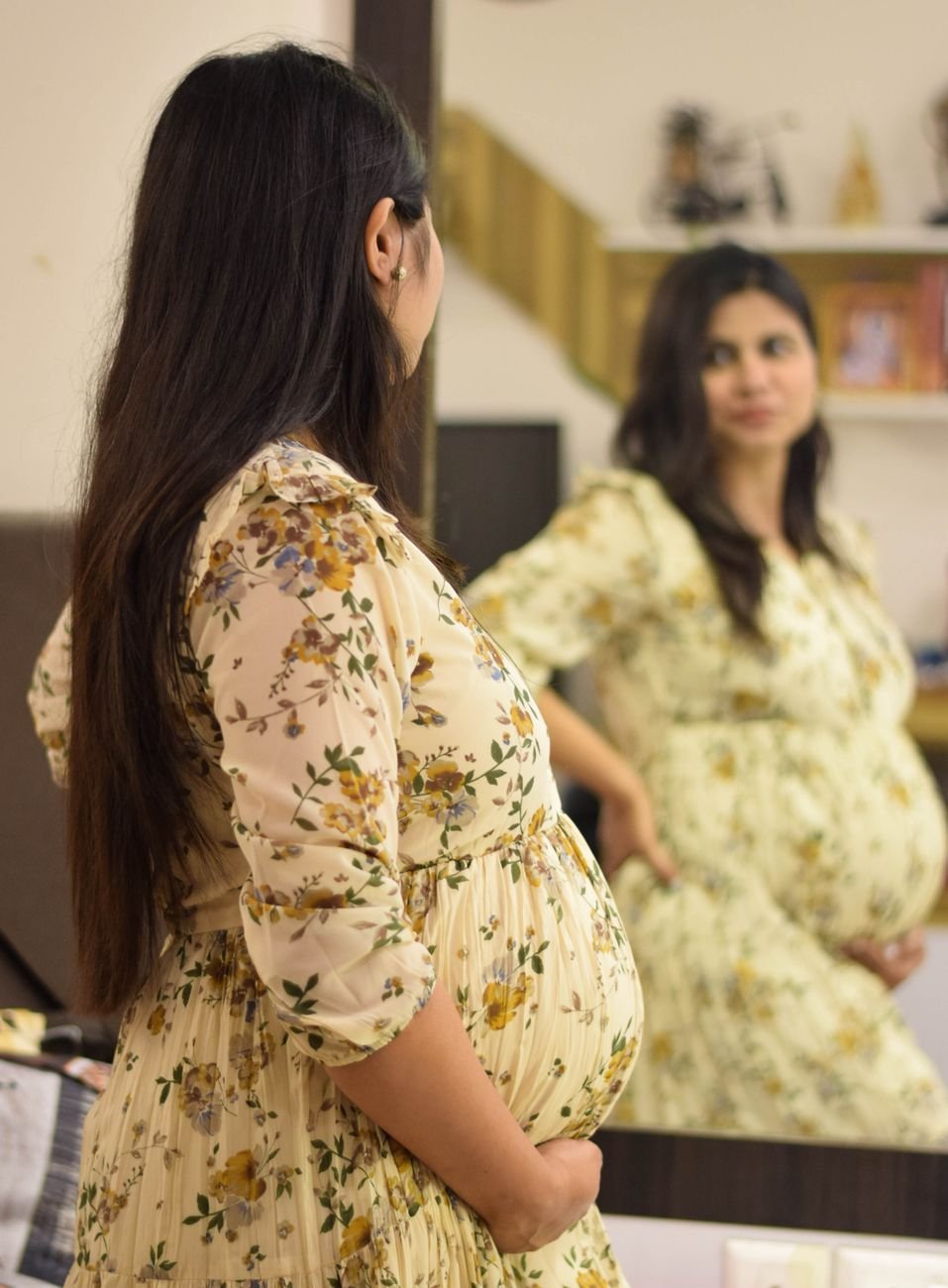 pregnant woman in floral dress standing in front of the mirror