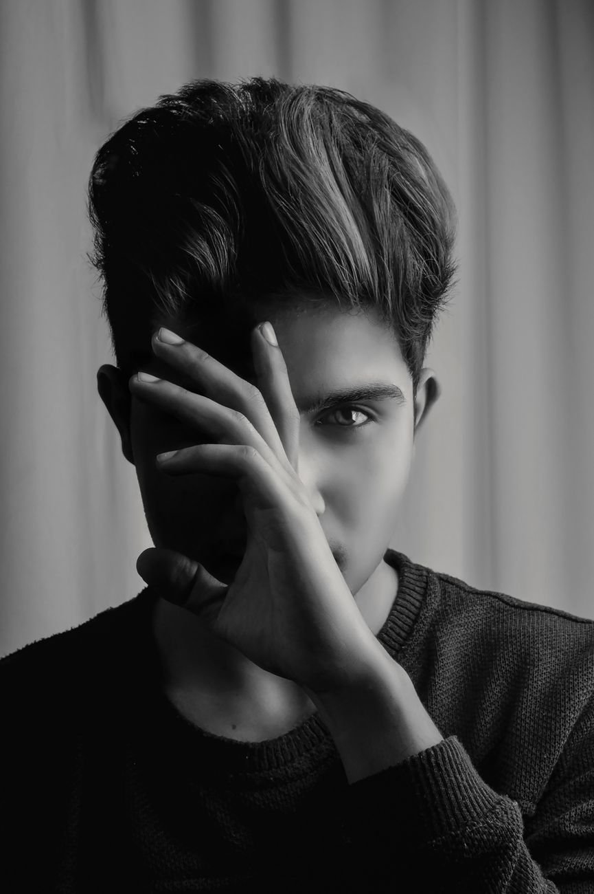 grayscale portrait photo of man posing with hand hiding part of his face