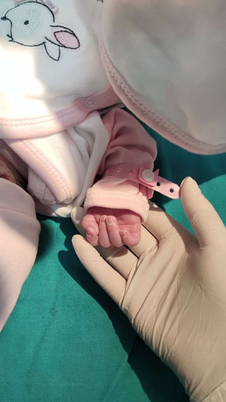 newborn in pink outfit holding gloved hand