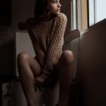 serious young ethnic female sitting near window in kitchen