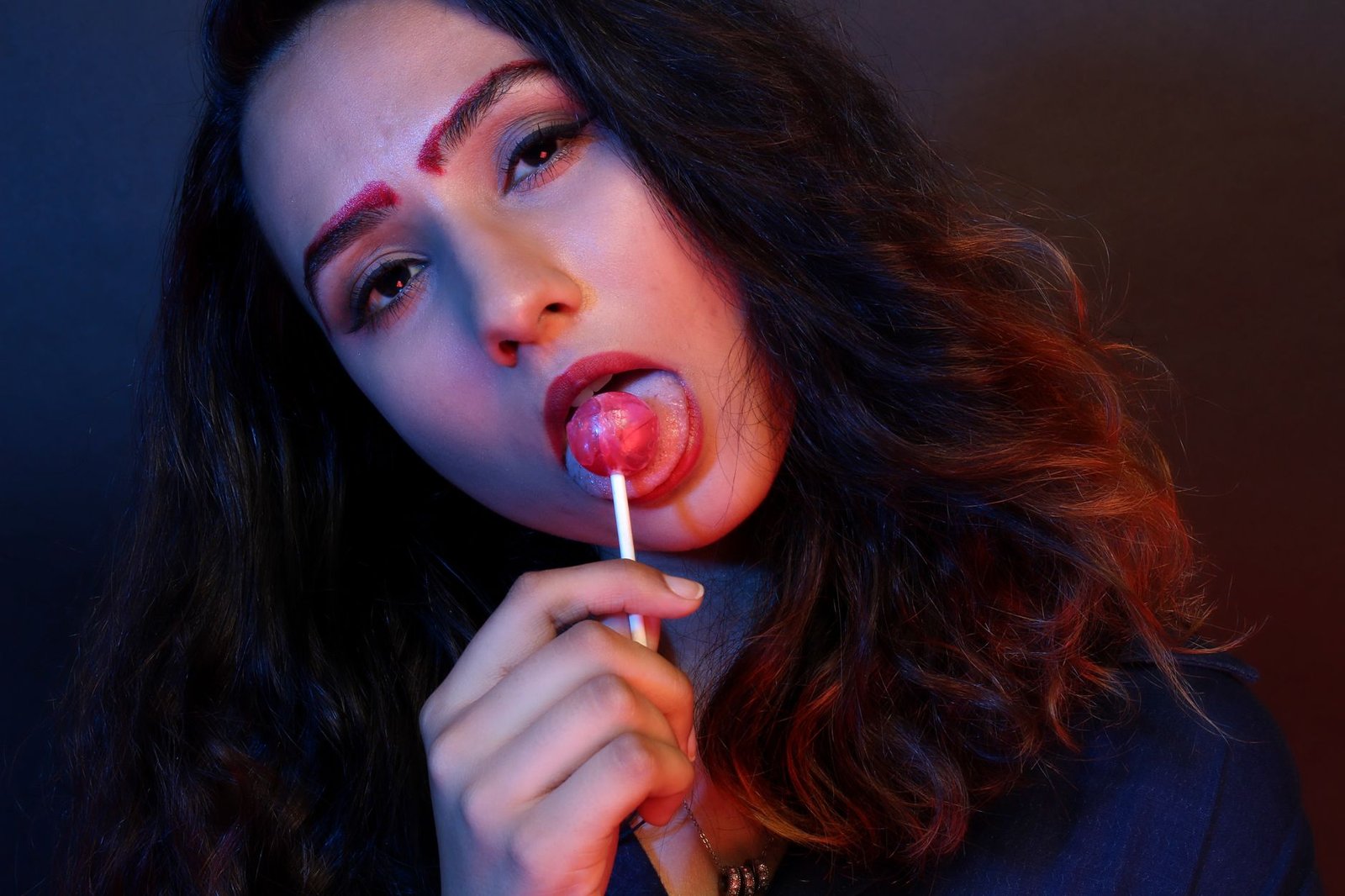 woman in blue top licking pink lollipop candy low light photography