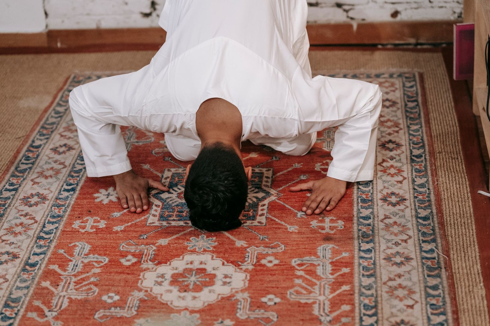 man in white thobe bowing down on red and blue rug
