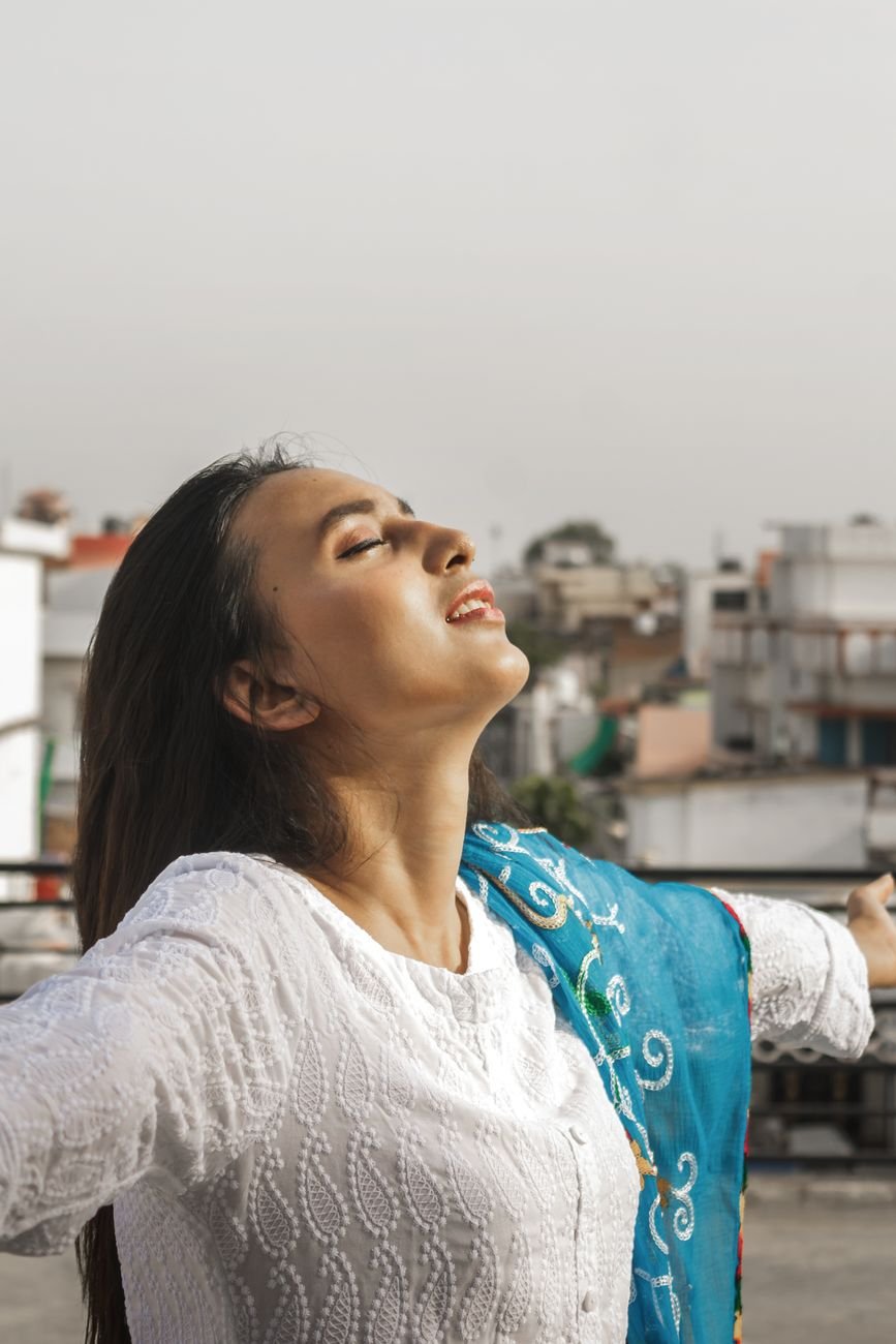 woman in white shirt and blue scarf with eyes closed and spreading arms