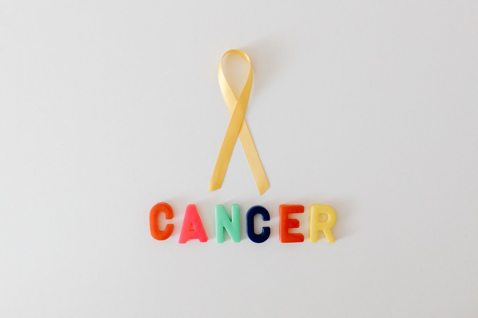 yellow ribbon over word cancer made of colorful letters